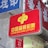 A red sign displaying the text 'China Welfare Lottery' in both Chinese and English, mounted on the exterior of a building. The surroundings include a blue sign with Chinese characters and a partial tree trunk visible on the right side.