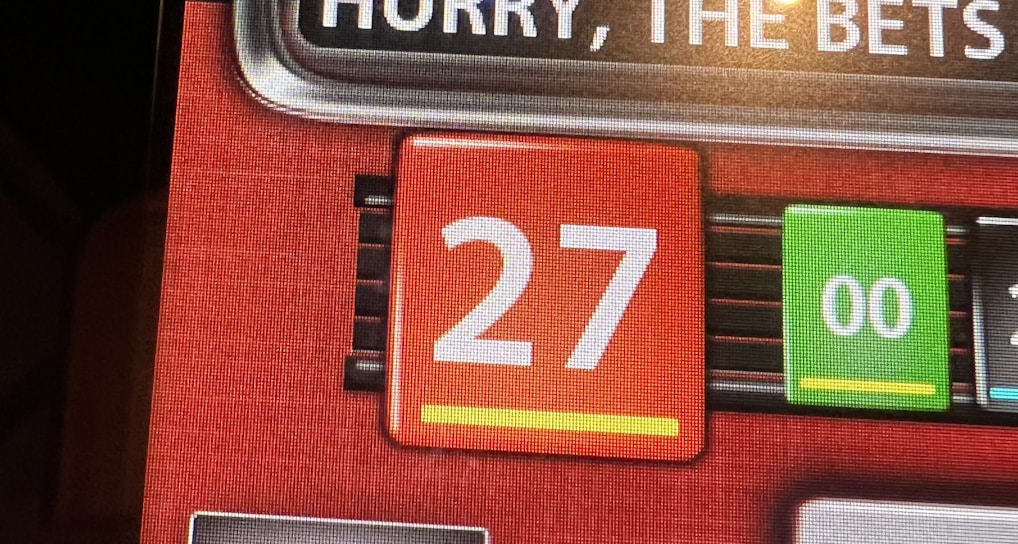 A digital display screen showing a casino betting interface, with text prompting to hurry bets and a highlighted number 27 in red. There are options for betting amounts and a 'share bets' button.